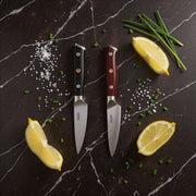 Two knives on a dark marble surface with lemon slices and herbs.