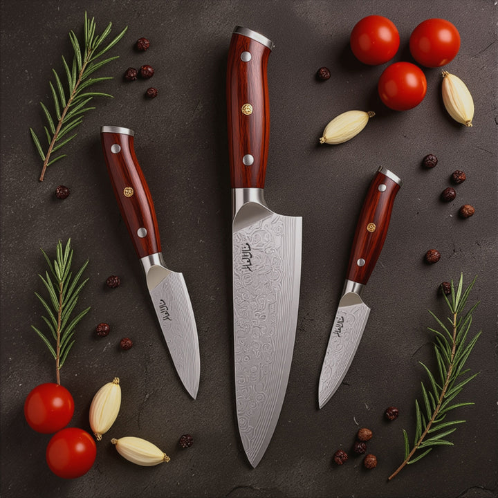 Set of three knives with red handles on a dark surface with vegetables and herbs.